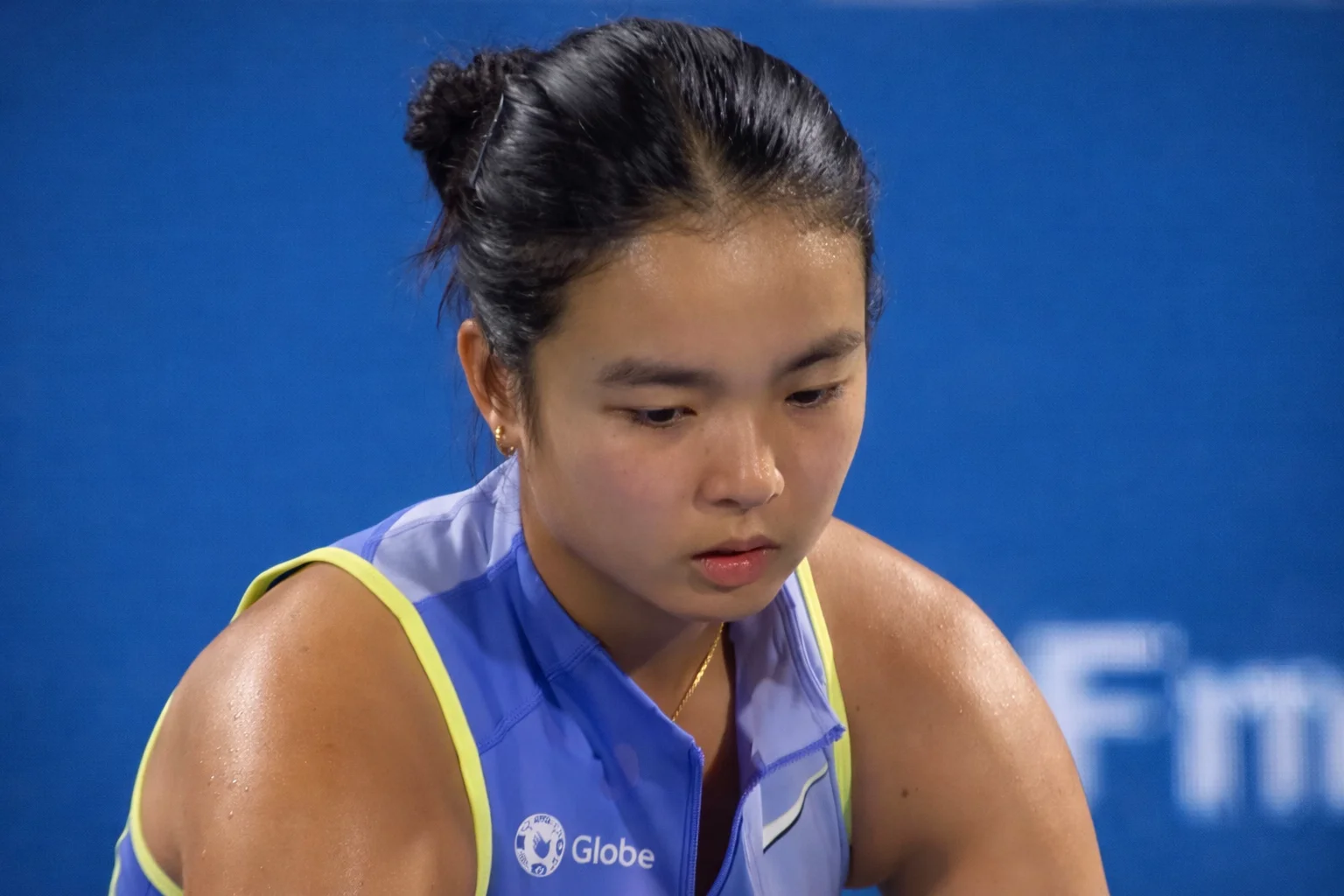 Close-up of a focused young East Asian Alexandra Eala in a blue sleeveless top with neon yellow trim during a hard-court match.