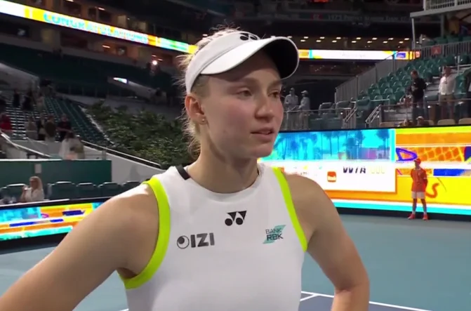 Elena Rybakina speaks during a post-match interview at the Miami Open, standing on court in her white tennis outfi
