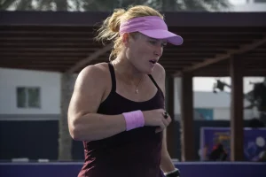 Peyton Stearns competing on court wearing a pink visor and burgundy outfit during a WTA tennis match.