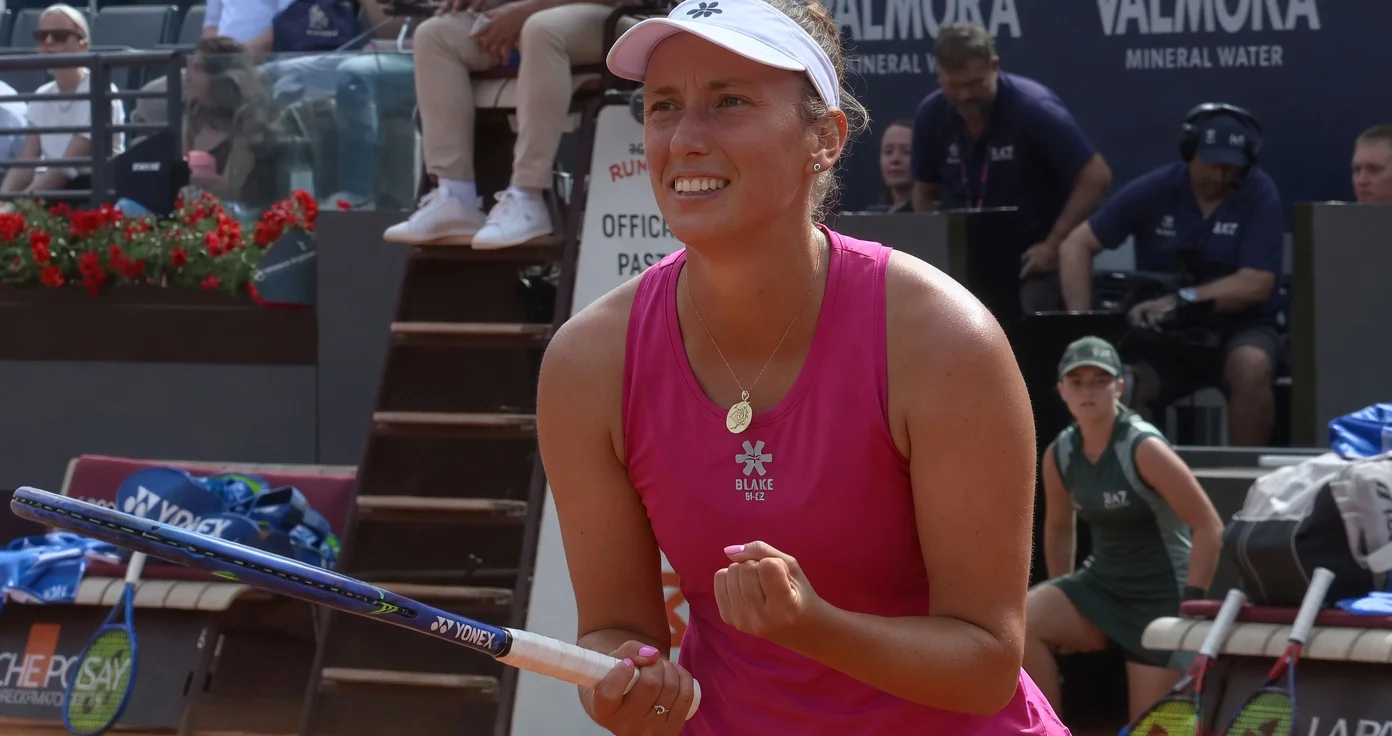 Elise Mertens celebrates victory over Jasmine Paolini at the Italian Open in Rome, wearing pink top and white visor while holding her tennis racket