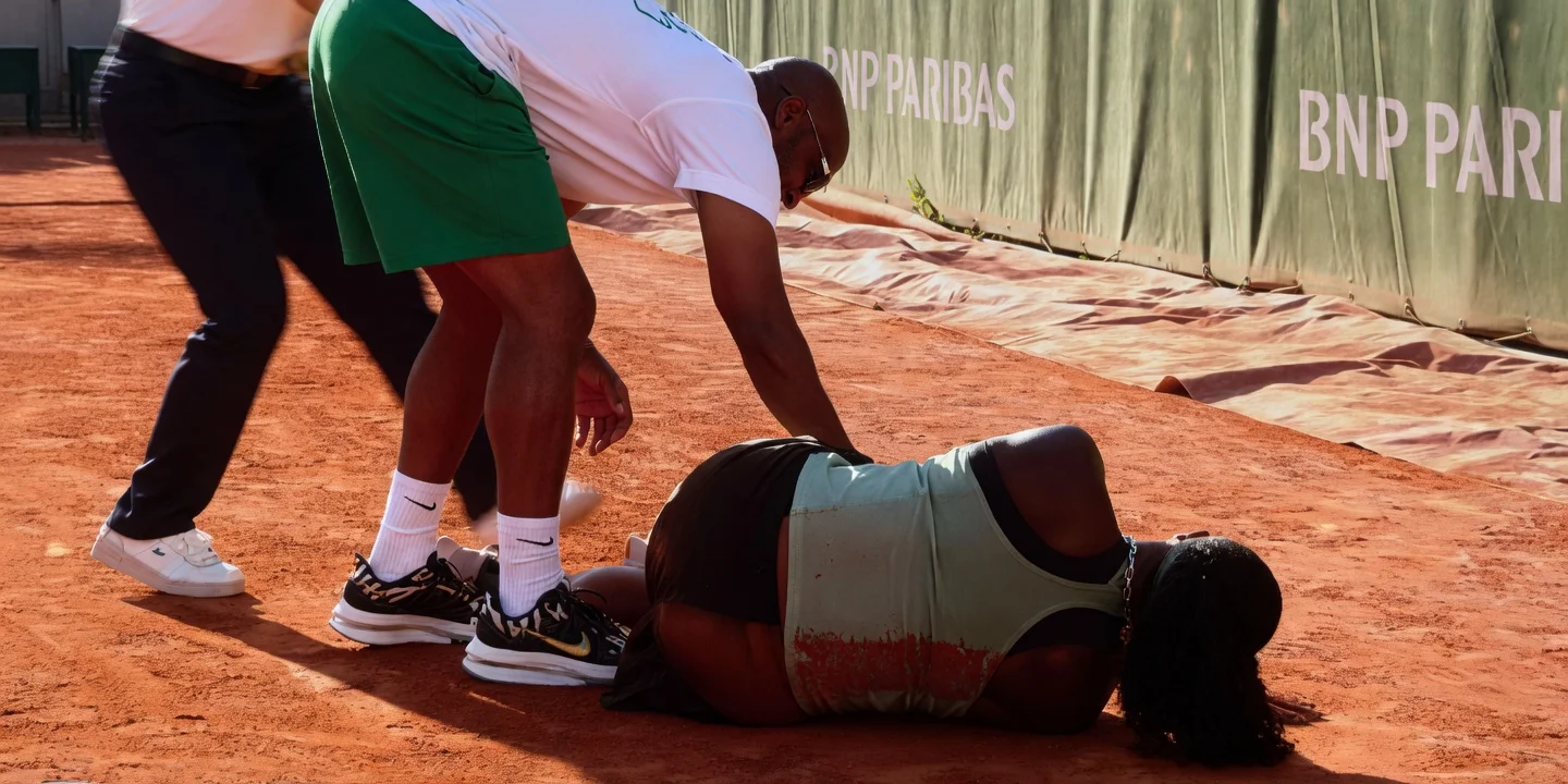 Hailey Baptiste lies on the red clay court at Roland Garros 2026 after injuring her left foot as her father bends down to assist her during the French Open match.
