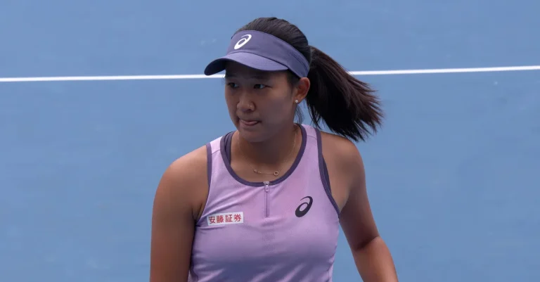 Moyuka Uchijima, Japanese professional tennis player, focused expression during a match on a blue hard court, wearing a purple Asics tennis outfit and visor