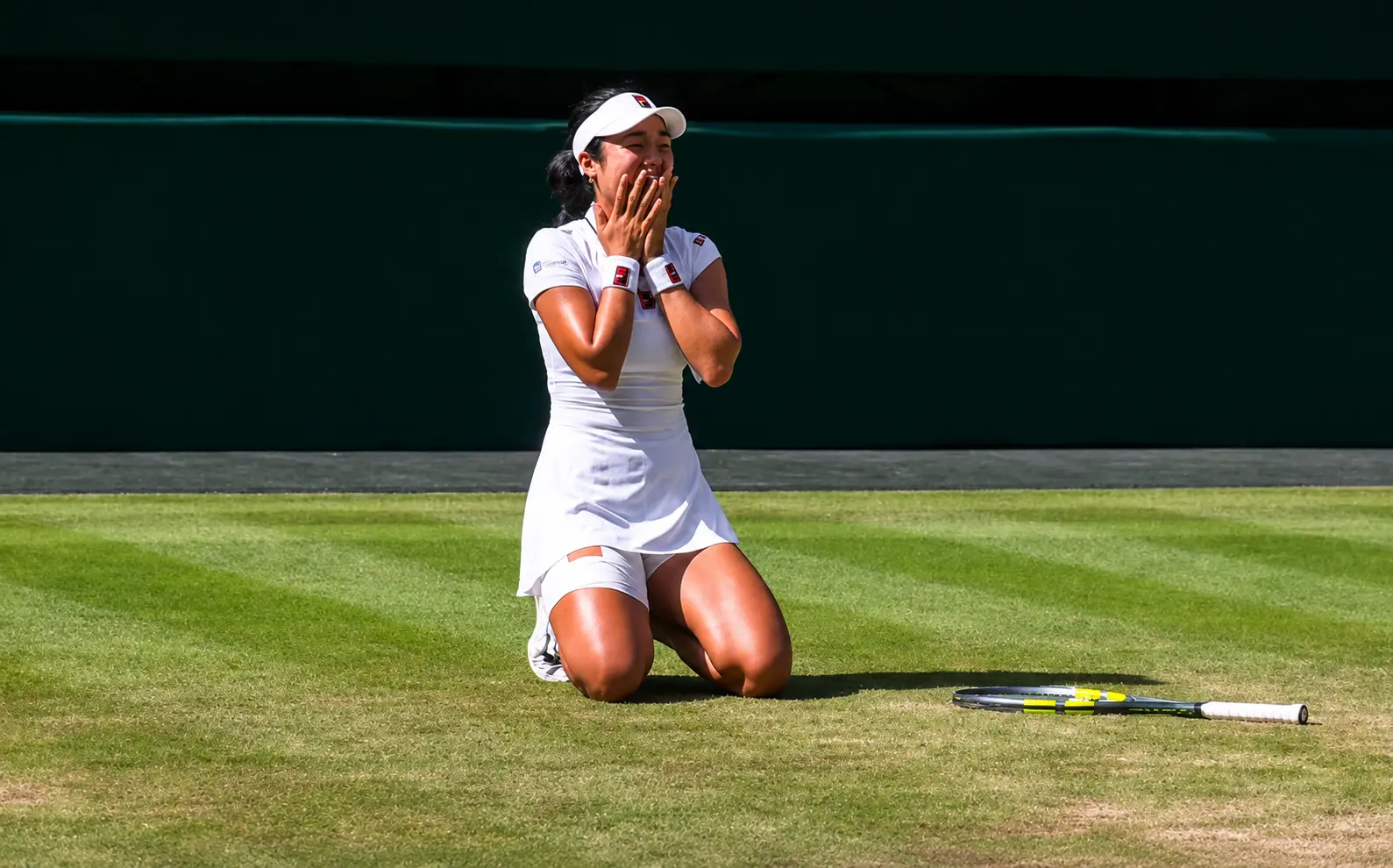 Alexandra Eala celebrates an emotional victory while kneeling on the grass during her Wimbledon 2026 women's singles match.